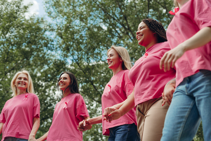 Women holding hands and wearing pink ribbons are walking for breast cancer awareness stock photo