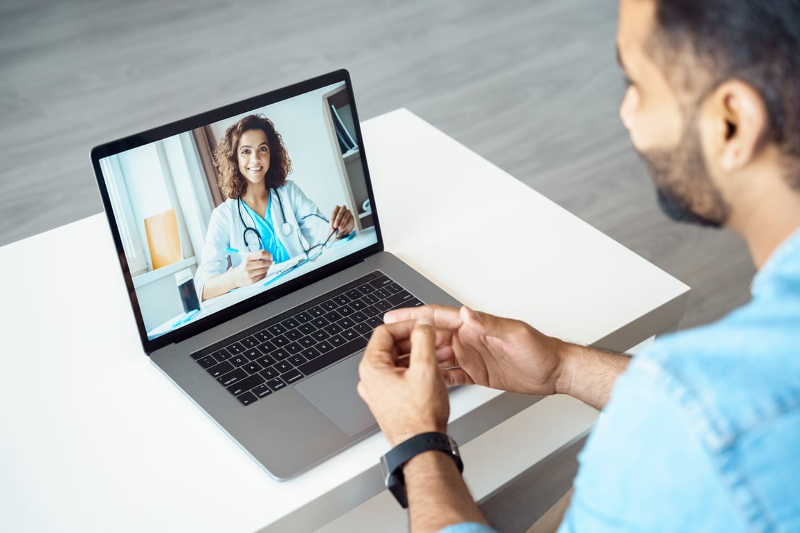 Young male adult patinet using laptop for a video telemedicine call with female doctor