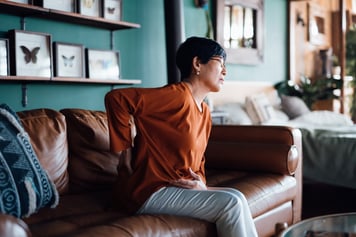 Woman sitting on brown sofa suffering from lower back pain