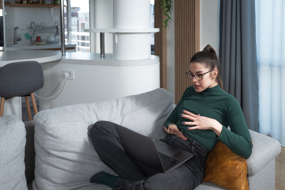 Woman using laptop on telemedicine video call while sitting on sofa