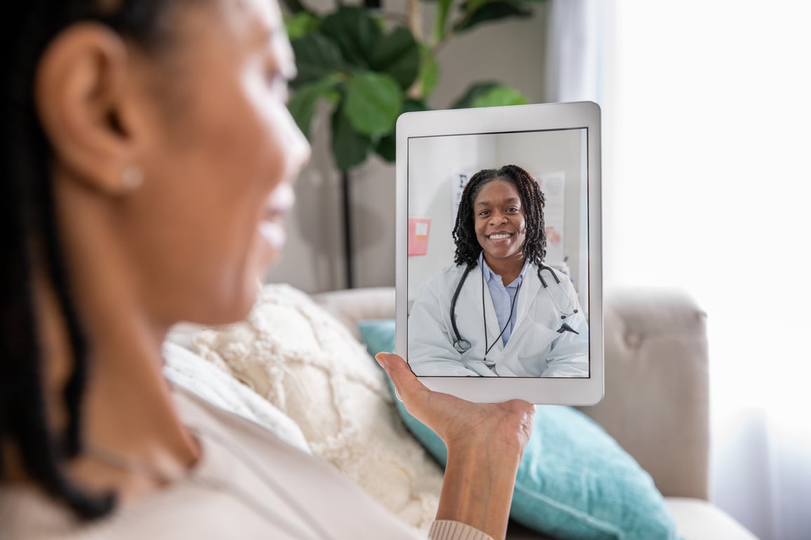 Woman using a tablet for video telemedicine call with smiling female doctor in white labcoat